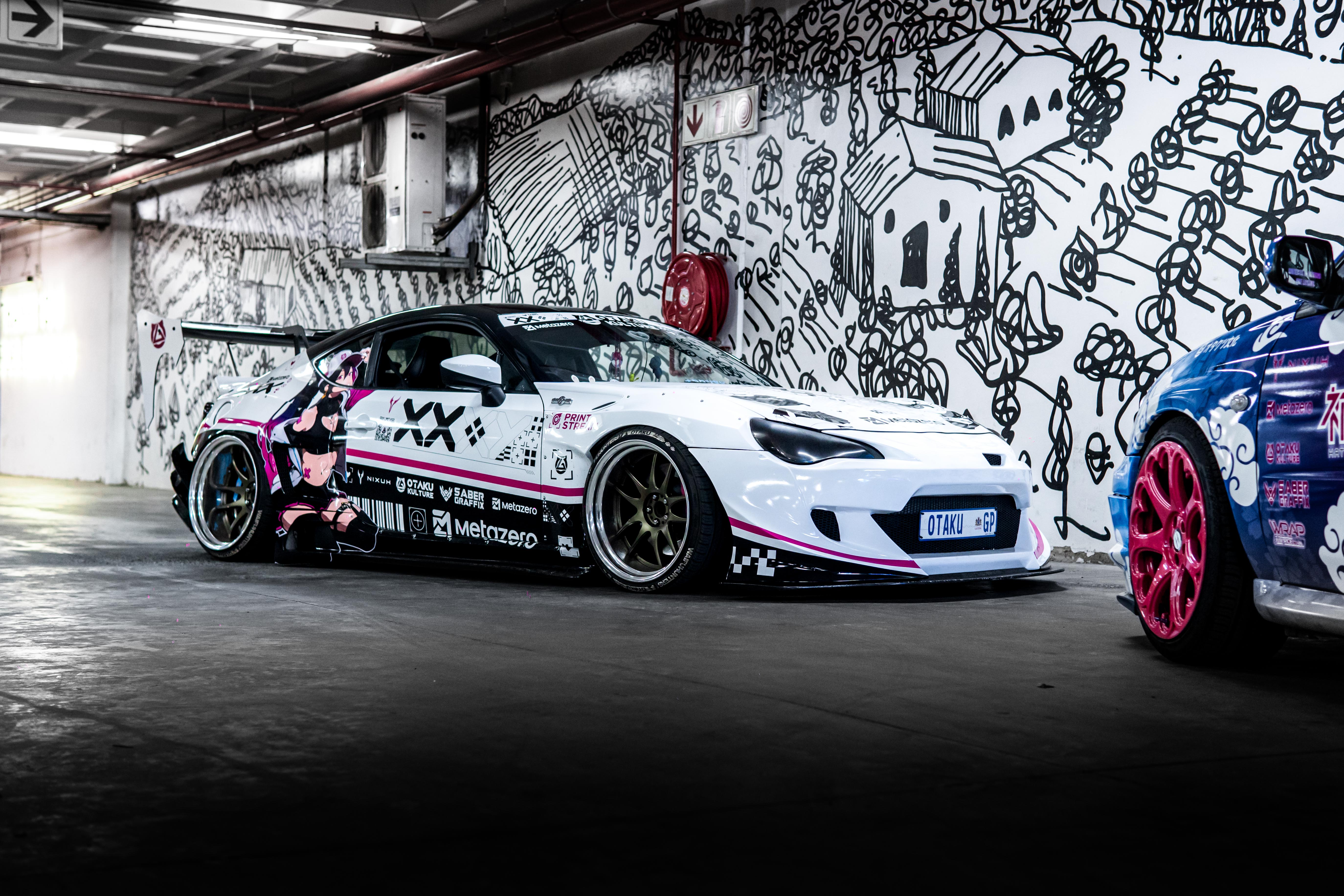 White sports car with pink accents parked in a garage with graffiti wall.