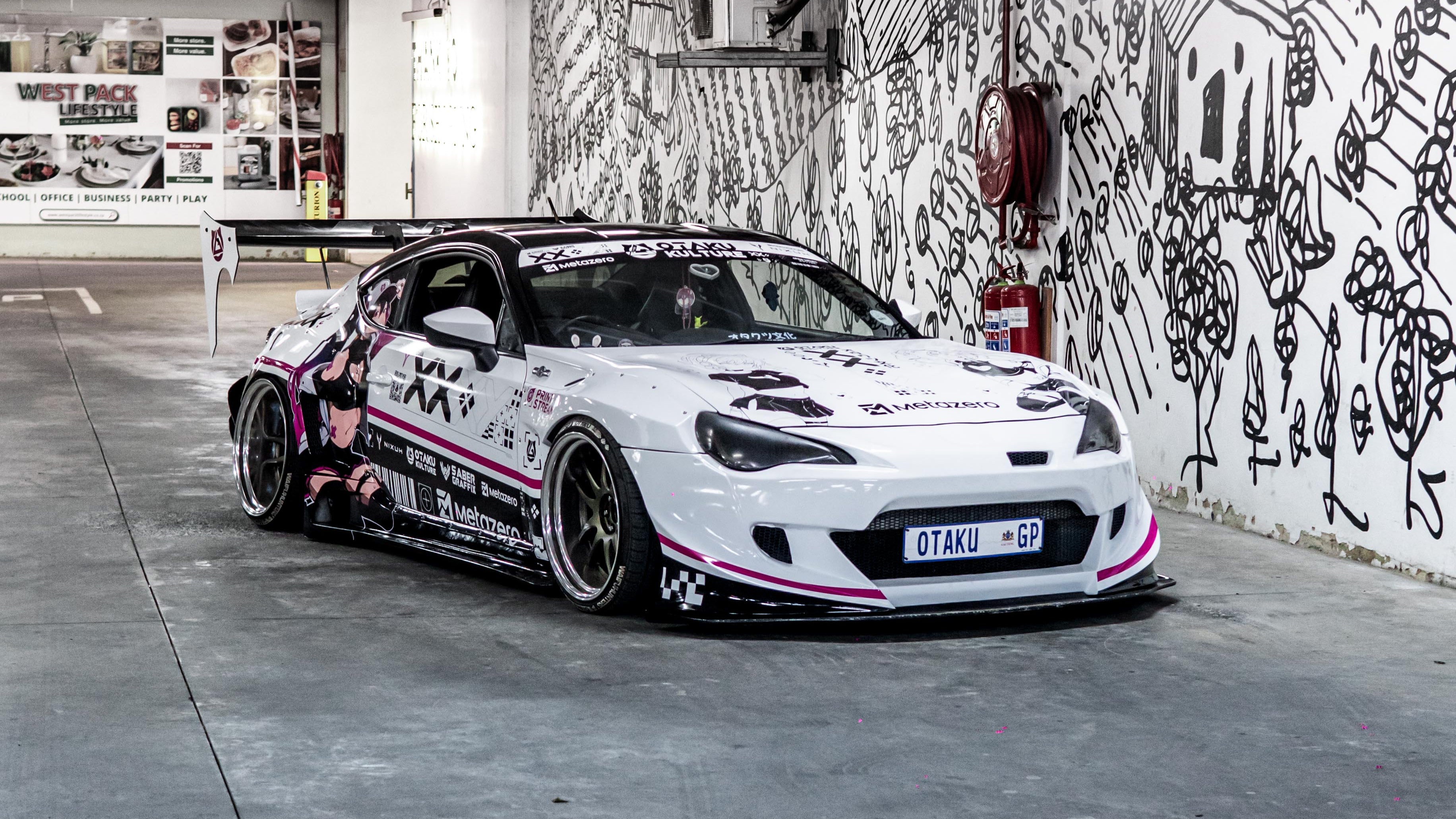 Black and White Toyota 86 with a rocket bunny body kit with pink accents in a garage with graffiti on the wall