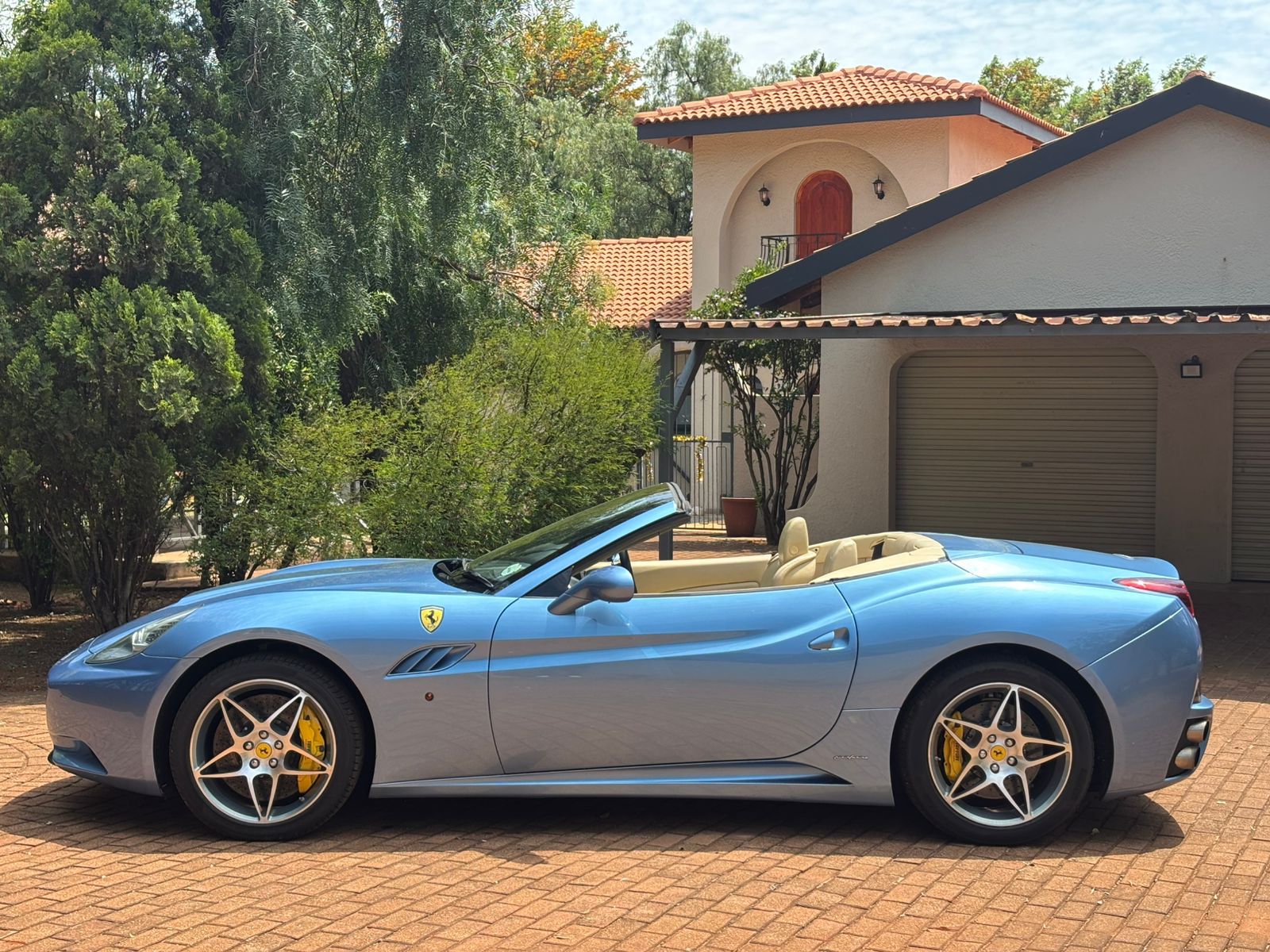 Blue convertible sports car parked on a driveway with a house in the background