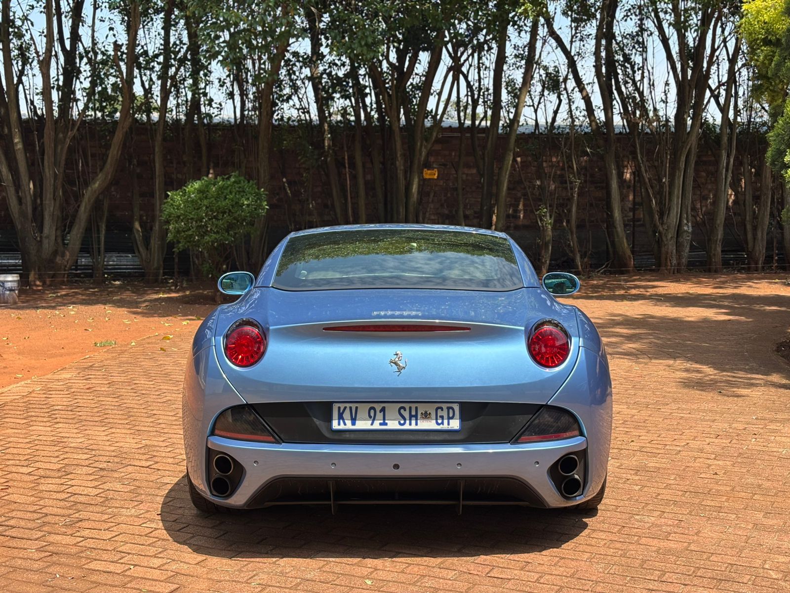Blue Ferrari car parked on a brick driveway with trees in the background